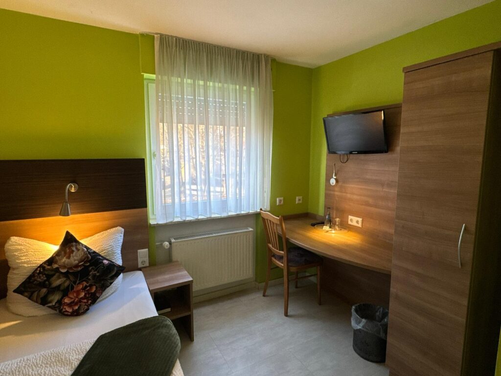 Einzelzimmer mit Schreibtisch, Fernseher und Kleiderschrank